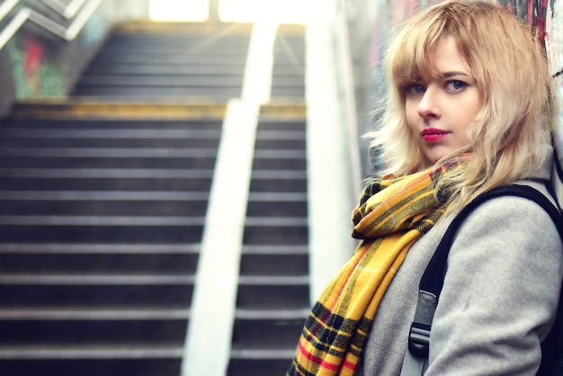 Schönes blondes Mädchen, das in der Nähe einer Wand mit Graffiti in einer unterirdischen Passage steht