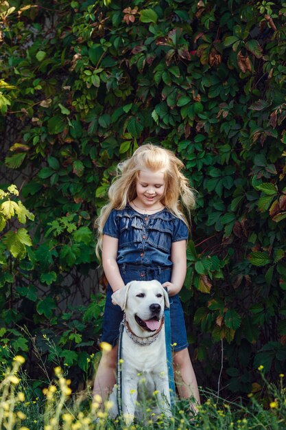 Schönes blondes Mädchen, das mit ihrem Hund spielt. Porträt im Freien. Serie