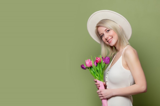 Schönes blondes Mädchen im weißen Hut und im Kleid mit Tulpen
