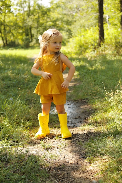 Schönes blondes Mädchen in einem Leinenanzug und gelben Stiefeln im Park