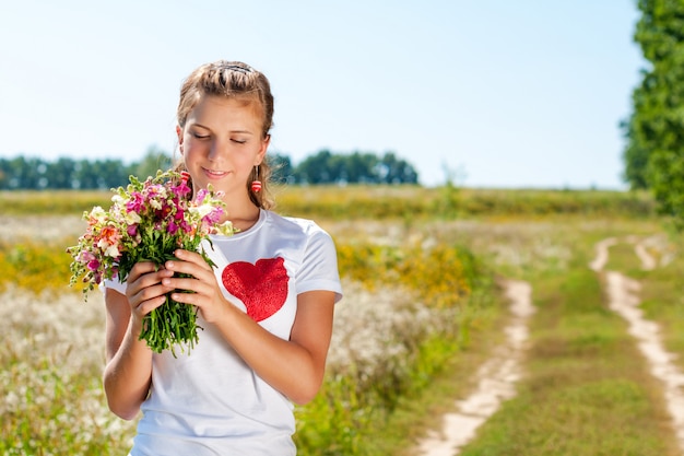 Schönes blondes Mädchen mit einem Blumenstrauß der wilden Blumen im Freien