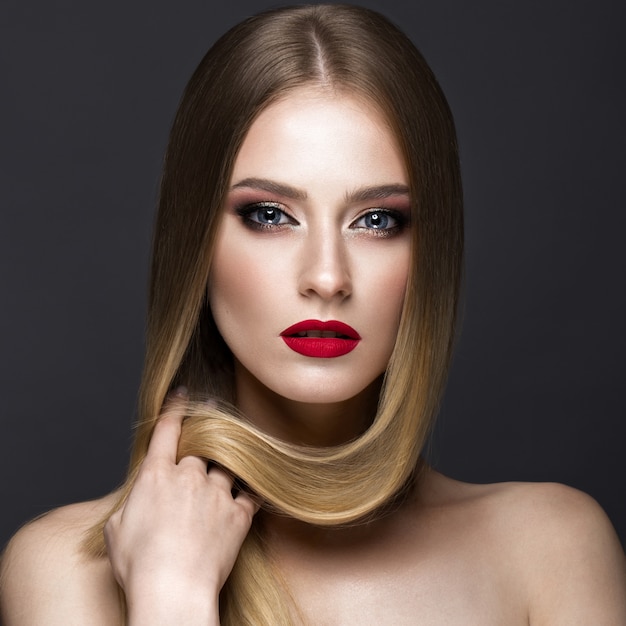 Schönes blondes Mädchen mit einem tadellos glatten Haar, einem klassischen Make-up und roten Lippen. Beauty Gesicht