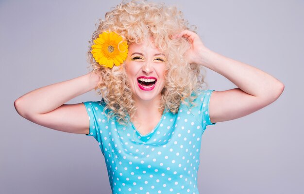 Schönes blondes Mädchen mit voluminöser lockiger Frisur, in einer blauen gepunkteten Bluse