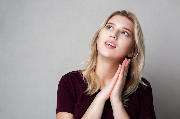 Schönes blondes Mädchen träumt. Studioaufnahme auf grauem Hintergrund. Freiraum