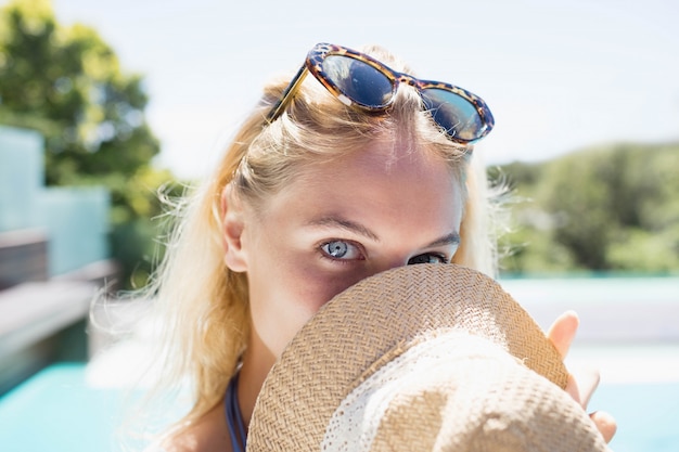 Schönes blondes versteckendes Gesicht mit Hut Poolside