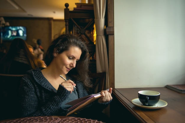 Schönes braunhaariges junges Mädchen, das in einem Café sitzt und einen Cappuccino trinkt.