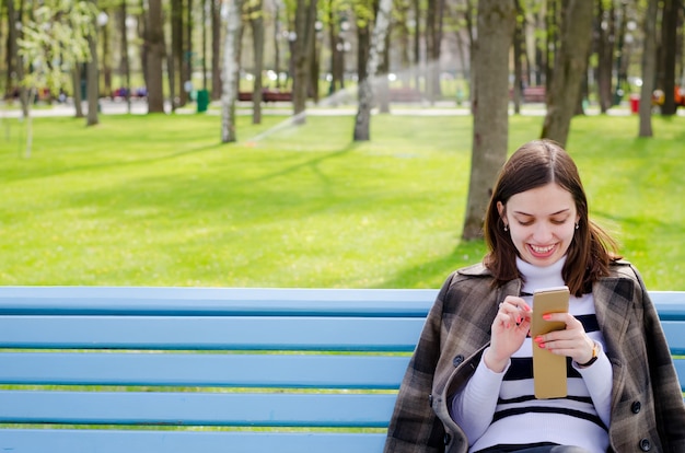 Schönes Brinette-Mädchen, das auf einer Bank sitzt, träumt und schreibt ihre Pläne in einem Notizbuch, Entspannen in einem Park an einem sonnigen Frühlingstag