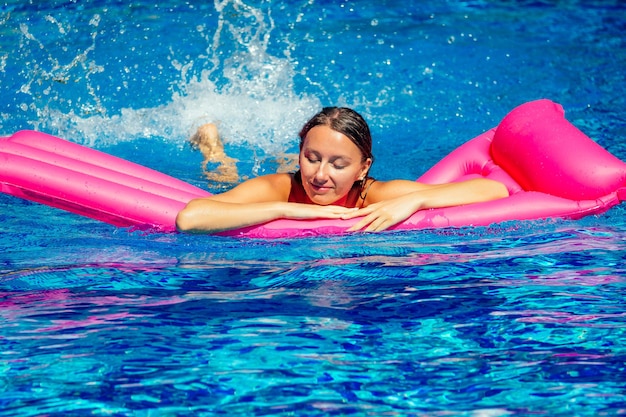 Schönes brünettes mädchen, das auf matratzen im pool schwimmt. fitnessfrauenmodell im schwarzen bikini, der am hotelpool ruht. diät-, sport- und bodybuildingkonzept wassergymnastik