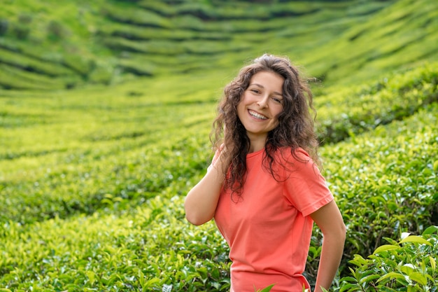 Schönes brünettes Mädchen, das in der Mitte des Teetals zwischen grünen Teebüschen aufwirft.