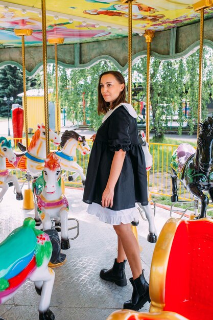 Foto schönes brünettes mädchen in einem schwarzen kleid posiert auf einem hellen karussell mit pferden