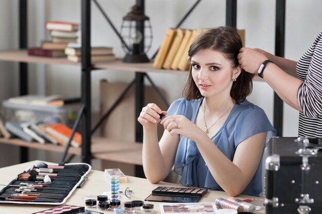 Schönes brünettes Modell, das im Ankleidezimmer am Tisch mit Make-up-Kosmetik sitzt