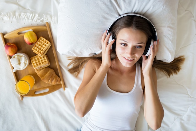 Schönes Brunettemädchen, das Musik auf Kopfhörern im Bett hört