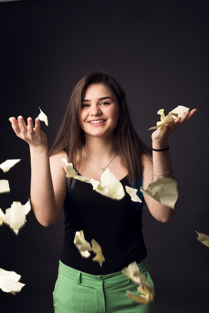 Schönes Brunettemädchen in den Gläsern und in den grünen Hosen mit Papieren