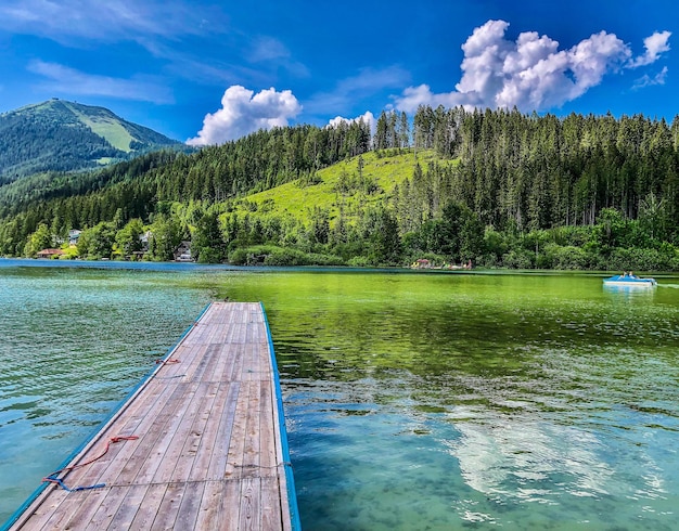 Schönes Dock-Anblick auf den See im Wald gegen den Himmel zwischen den Hügeln der Alpen