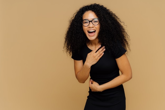 Schönes dunkelhäutiges Model kann nicht aufhören zu lachen, hört Comic-Geschichten, hält die Hand am Bauch