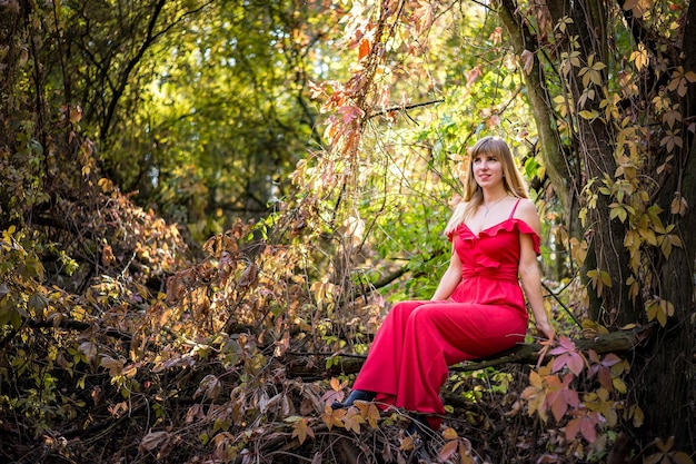 Schönes Elfenmädchen in rotem Kleid im Herbstwaldwald-Fantasiemärchen