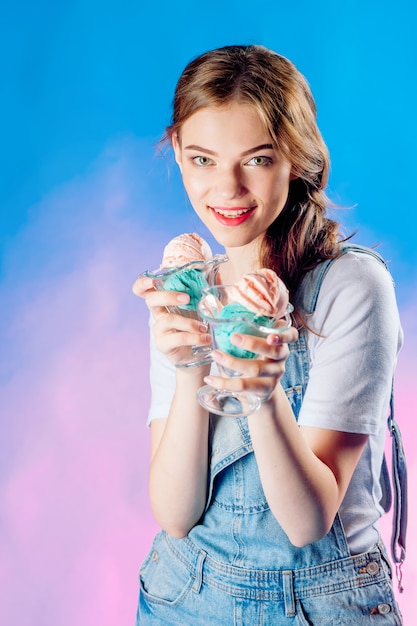 Schönes emotionales Mädchen auf einem blauen Hintergrund hält in ihren Händen eine köstliche rosa Eiscreme. süßes Verkaufskonzept, Verkauf