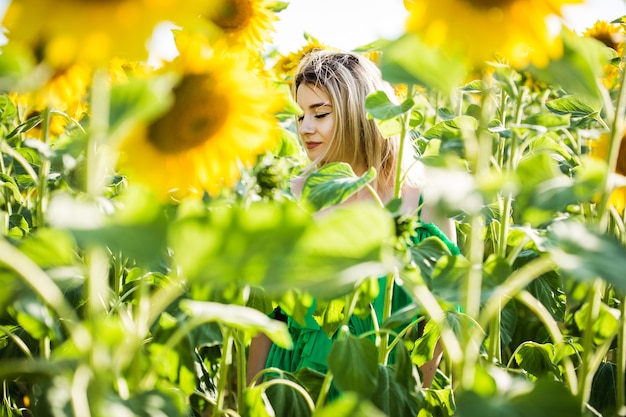 Schönes europäisches Mädchen in einem grünen Kleid auf Natur mit Sonnenblumen