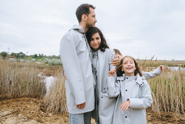 Schönes Familienportrait gekleidet im Regenmantel nahe dem See