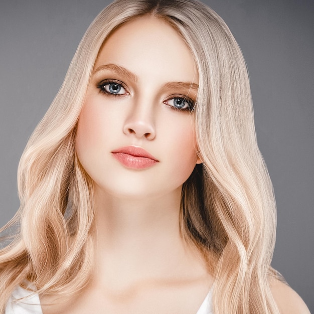 Schönes Frauen-Gesichts-Porträt-Schönheits-Hautpflege-Konzept mit dem langen blonden Haar. Fashion Beauty Model mit schöner Frisur auf grauem Hintergrund