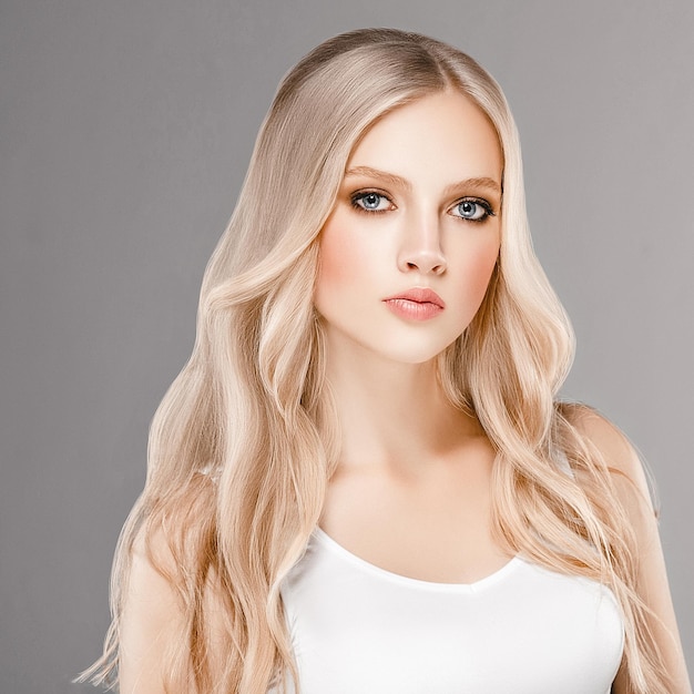 Schönes Frauen-Gesichts-Porträt-Schönheits-Hautpflege-Konzept mit dem langen blonden Haar. Fashion Beauty Model mit schöner Frisur auf grauem Hintergrund