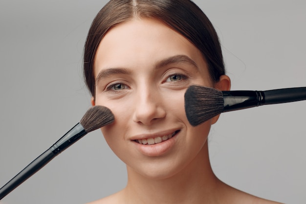 Schönes Frauengesicht mit natürlichem Make-up. Hand des Make-up-Meisters mit Pinsel. Junge Schönheitsmodell weiblich. Make-up in Bearbeitung.