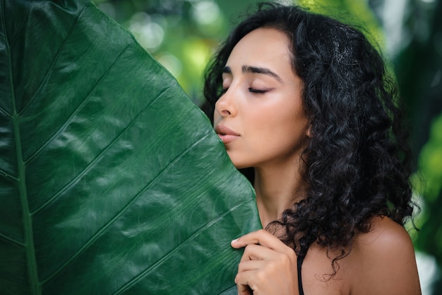 Schönes Frauengesicht mit natürlichem Nude-Make-up auf einer tropischen Blattoberfläche