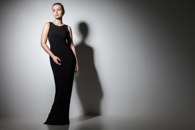 Schönes Frauenmodel posiert im eleganten schwarzen Kleid im Studio