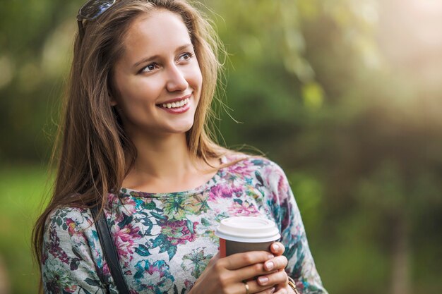 Schönes Frauenmodell mit Kaffee zum Mitnehmen im Park. Stil, lässig, trinken, Glück, sonnig