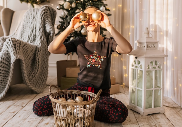 Schönes fröhliches glückliches junges Mädchen auf dem Boden im Schlafanzug mit Weihnachtsspielzeug nahe dem Neujahrsbaum zu Hause