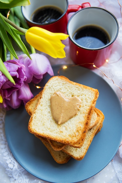 Schönes Frühstück im Bett. Schwarzer Kaffee, leuchtende Blumen, Toast mit Erdnussbutter. Nahansicht.