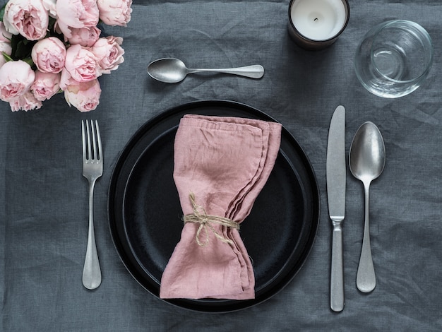 Schönes Gedeck mit rosa Sprayrosen und -kerze auf grauer Leinentischdecke.