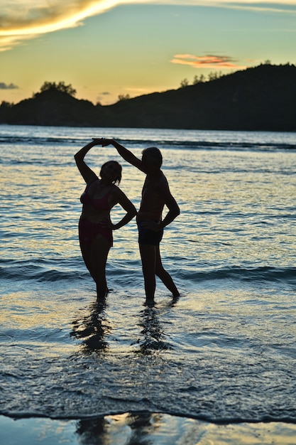 Schönes glückliches älteres Paar, das bei Sonnenuntergang am Strand im tropischen Resort tanzt?