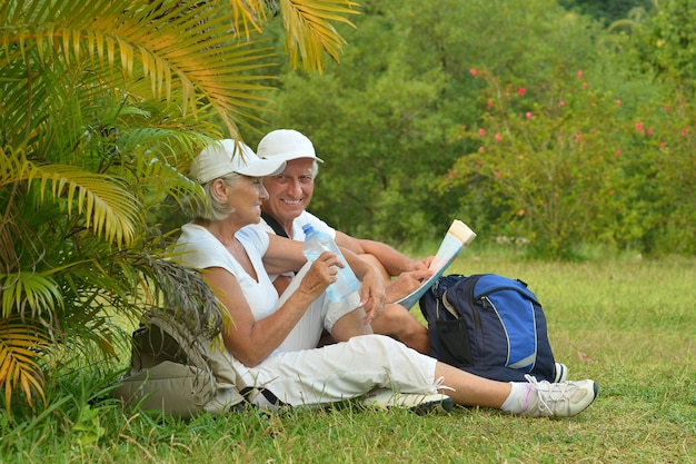 Schönes glückliches älteres Paar ruht sich im tropischen Resort mit Rucksäcken und Karte aus