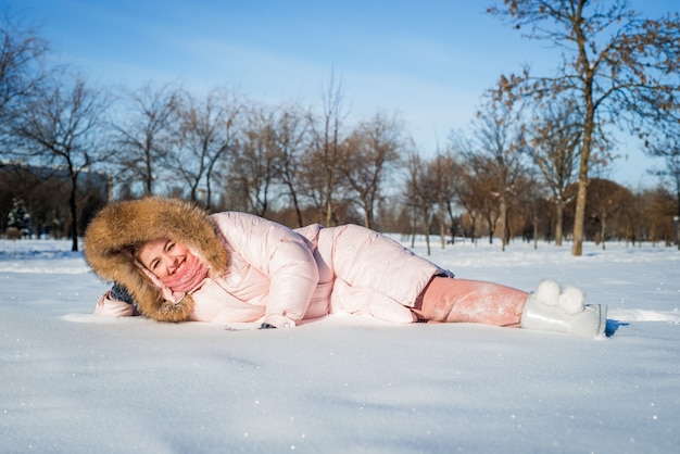 Schönes glückliches lachendes junges Mädchen, das Wintermütze, Schal mit Schneeflocken bedeckt trägt. Aktiver Lebensstil. Winterwaldlandschaftshintergrund.