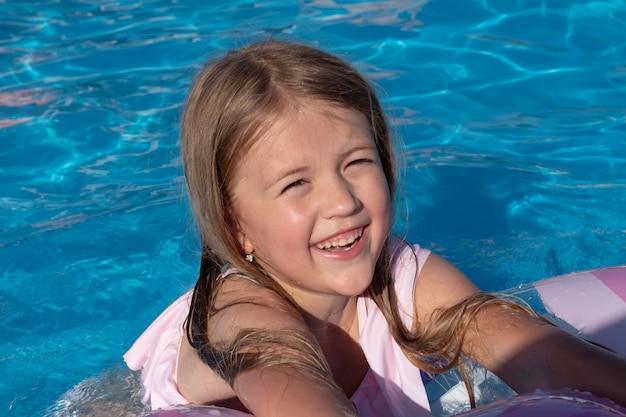 Schönes glückliches lächelndes kleines blondes Mädchen in einem rosa Badeanzug schwimmt im Pool
