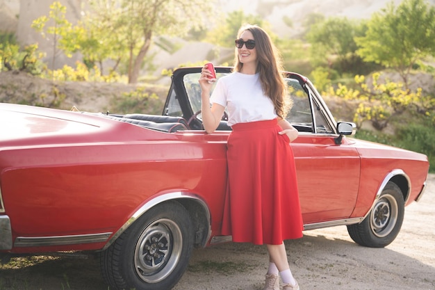 Foto schönes, glückliches mädchen in einem rock, das in der nähe eines retro-autos in den cappadocia-bergen mit einer dose getränk posiert