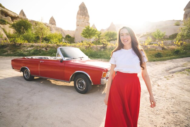 Schönes glückliches Mädchen in einem Rock posiert in der Nähe eines Retro-Autos in den Bergen von Kappadokien