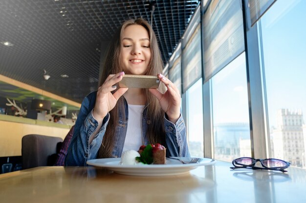 Schönes glückliches Mädchen macht Foto von Essen im Café, Latte auf dem Tisch, Desserteis Schokoladenkuchen Kirschminze