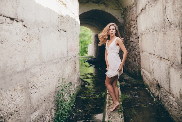 Schönes glückliches Mädchen mit lockigem natürlichem Haar im weißen Kleid tanzt im Tunnel. Sommerschönheitsporträt. Träumerin genießen die Natur.