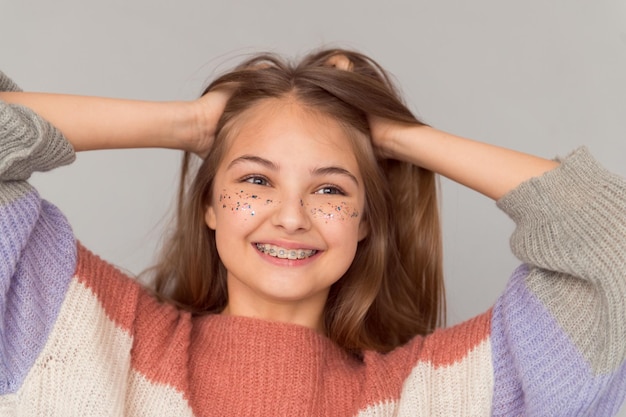 Schönes, glückliches Teenager-Mädchen mit glänzenden Sommersprossen im Gesicht und Hosenträgern, die den Kopf halten und lächeln