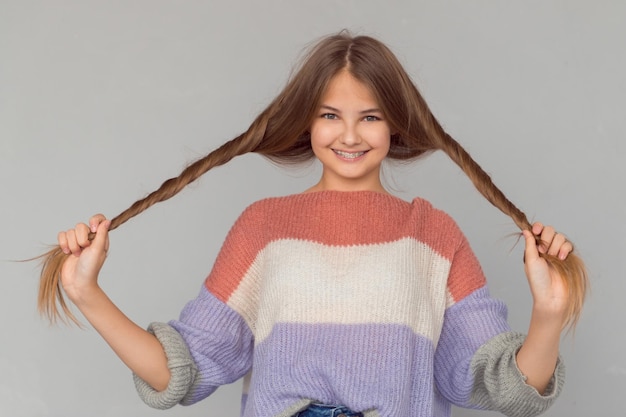 Schönes, glückliches Teenager-Mädchen mit glänzenden Sommersprossen im Gesicht und Hosenträgern, die Haare halten und lächeln