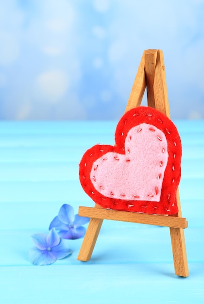 Schönes Herz kleine dekorative Staffelei auf blauem Hintergrund