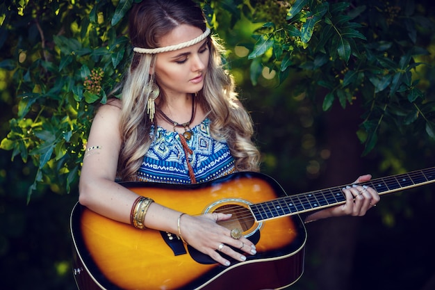 Schönes Hippie-Mädchen mit Gitarre im Park bei Sonnenuntergang