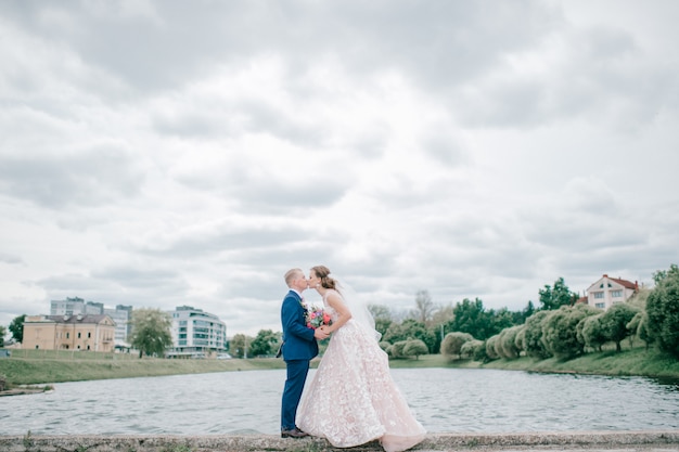 Schönes Hochzeitspaar, das mit See und Park auf Hintergrund aufwirft