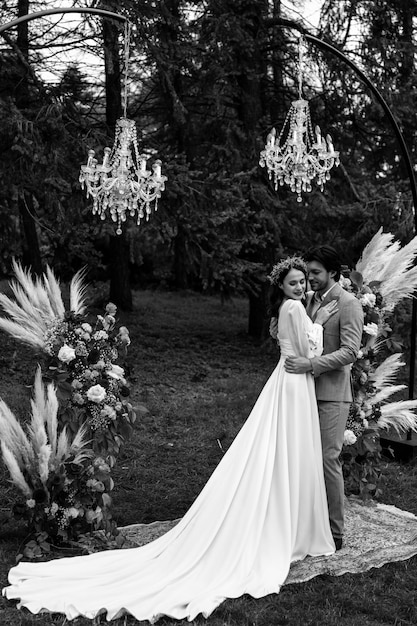 Schönes Hochzeitspaar, das sich bei der Hochzeitszeremonie auf dem Hintergrund des Waldes schwarz und w umarmt