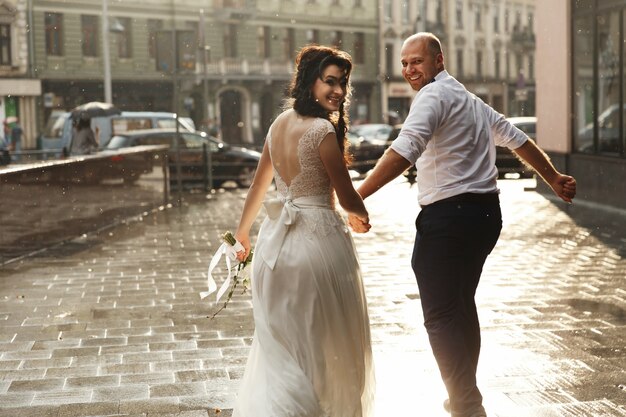 Schönes Hochzeitspaar schaut das glückliche Gehen um die Stadt im Regen