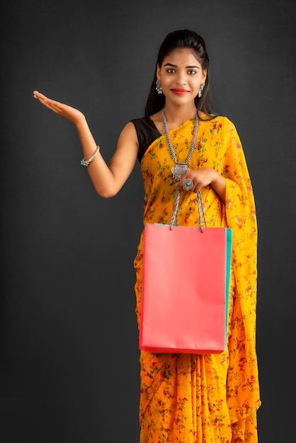 Schönes indisches junges Mädchen, das mit Einkaufstaschen auf einem grauen Hintergrund hält und aufwirft
