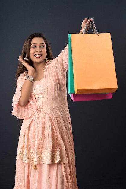 Schönes indisches junges Mädchen, das mit Einkaufstaschen auf einem grauen Hintergrund hält und aufwirft