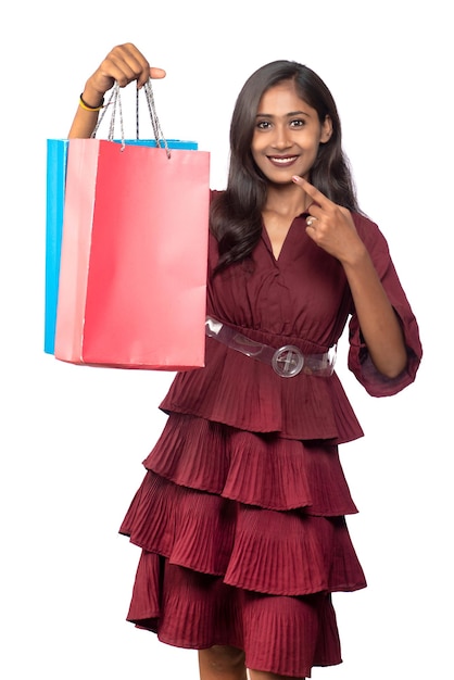 Schönes indisches junges Mädchen, das mit Einkaufstaschen auf einem weißen Hintergrund hält und aufwirft